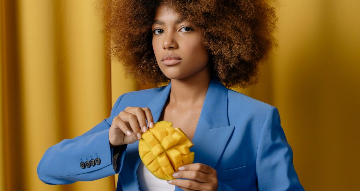 Kobieta w niebieskim żakiecie trzymająca w dłoniach ponacinane mango