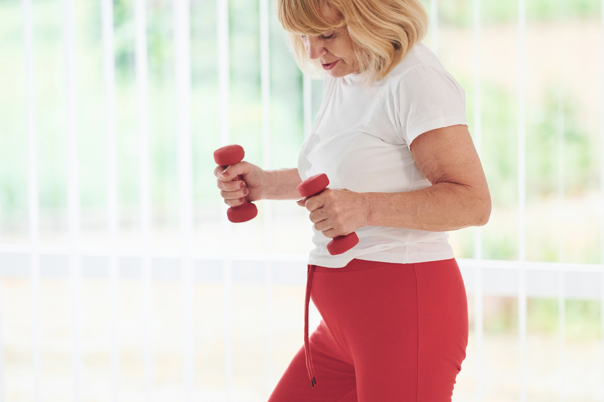 Na obrazku widać starszą panią, która ćwiczy w swoim domu. Pani wykonywany ćwiczenia skupiające się na poprawie elastyczności i siły mięśni oraz utrzymaniu zdrowego kręgosłupa. Ćwiczenia te można wykonywać w domu przy użyciu podstawowych przyborów, takich jak hantle, piłka gimnastyczna czy mata do ćwiczeń. Pani wydaje się być w dobrej formie fizycznej i pełnej energii, co pokazuje, że ludzie starsi mogą cieszyć się aktywnością fizyczną i zdrowym trybem życia. Obrazek może stanowić inspirację dla osób starszych, które chcą dbać o swoje zdrowie i kondycję fizyczną w domowym zaciszu.