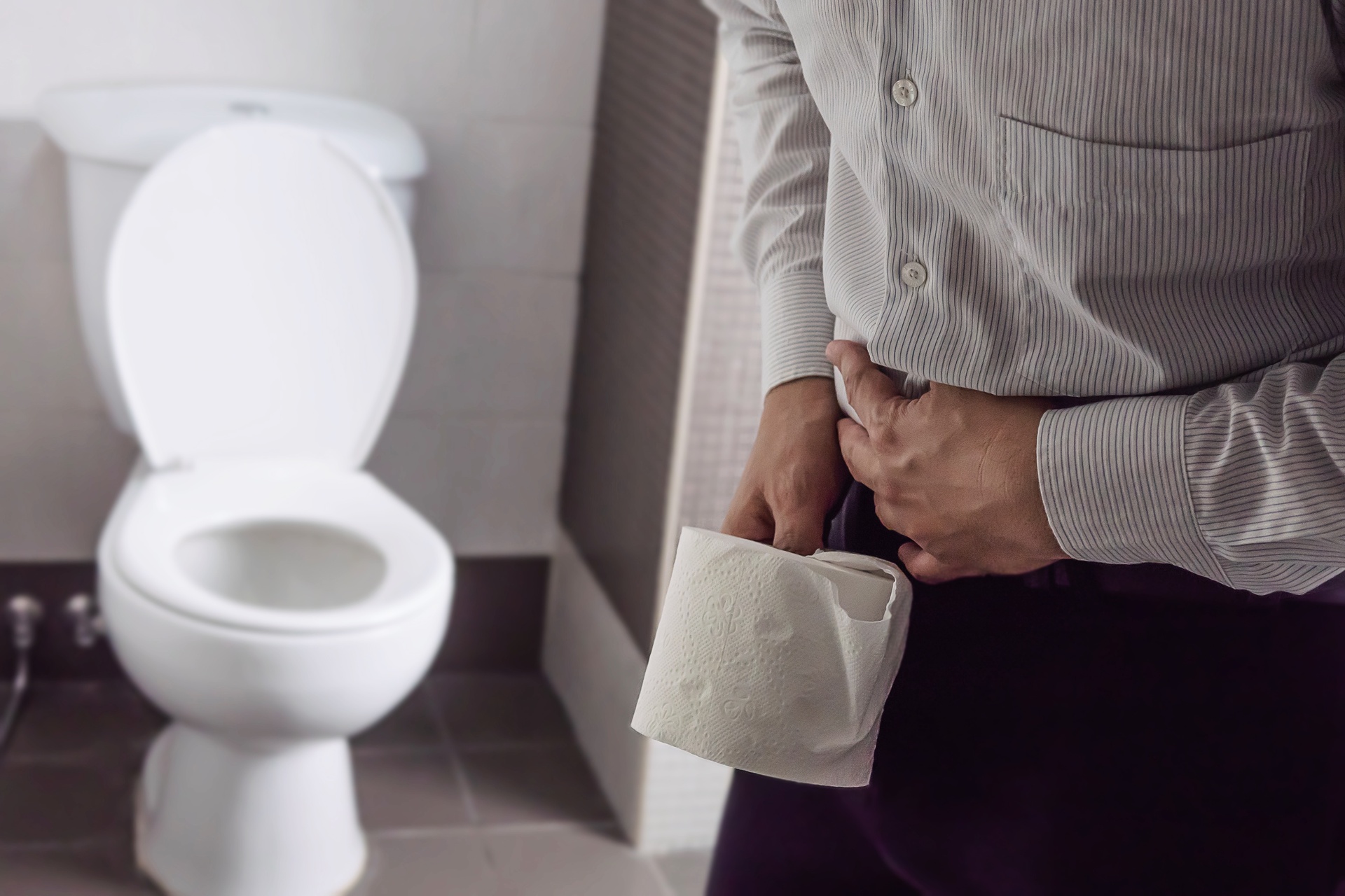 Na obrazku widać mężczyznę stojącego przy toalecie, trzymającego w ręce papier toaletowy, z problemem śluzu w kale. Jego wyraz twarzy wyraża zaniepokojenie i niepokój. Obrazek ukazuje trudności i dyskomfort, związane z obecnością śluzu w kale, oraz potrzebę podjęcia odpowiednich działań w celu rozwiązania tego problemu