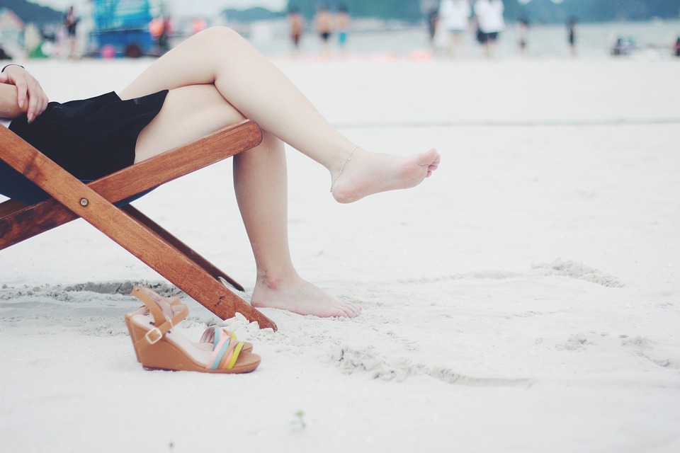 Kobieta z wyleczona ostrogą pietową siedzi na plaży bez butów