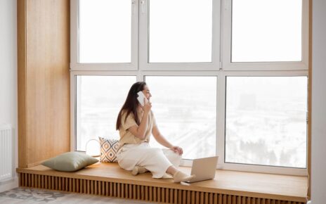 Kobieta stoi przy duych oknach w swoim salonie