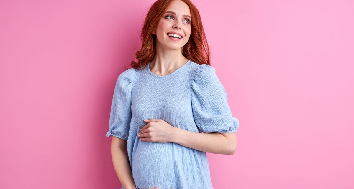 Kobieta w ciąży w nebieskiej sukience trzyma się za brzuch