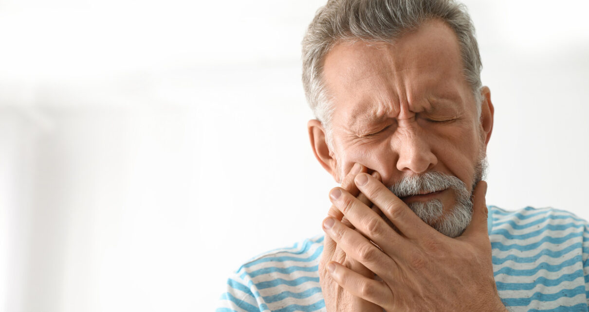 Zgorzel zęba - mężczyzna odczuwający ból zęba trzymający się za twarz