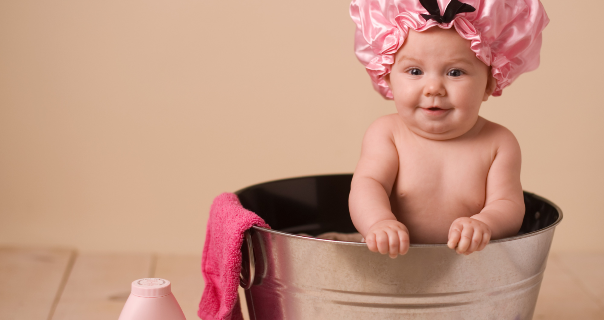 Małe dziecko siedzi w różowym czepku na głowie przed kąpielą