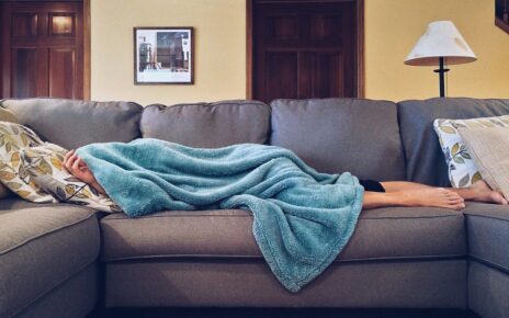 Przeziębiona kobieta leży na kanapie pod niebieskim kocem
