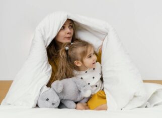 Kobieta z dzieckiem siedzi pod białą bawełnianą kołdrą