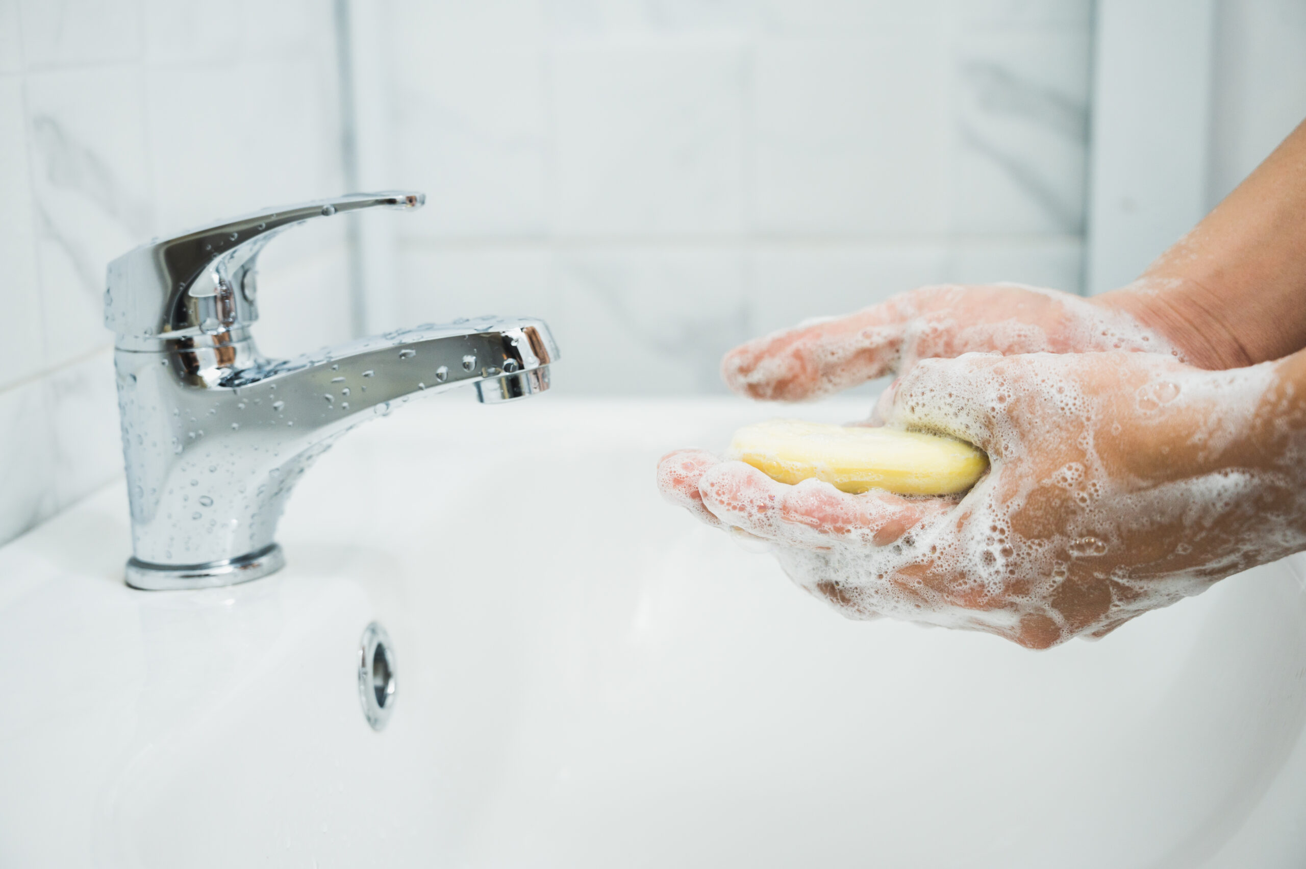 Na obrazku widać osobę stojącą przy umywalce i myjącą ręce. Używa ona płynu do mycia rąk i starannie spłukuje wodą, aby zapewnić odpowiednią higienę. Gest i wyraz twarzy świadczą o zaangażowaniu w proces mycia, co podkreśla znaczenie tego działania dla zdrowia i ochrony przed chorobami.