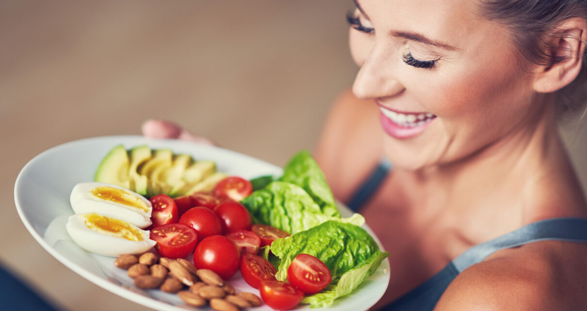 Na obrazku widzimy kobietę, która trzyma w rękach talerz z pysznym i zdrowym posiłkiem wegetariańskim. Na talerzu znajdują się różnorodne warzywa oraz zboża, co pozwala na dostarczenie organizmowi odpowiedniej dawki składników odżywczych. Kobieta uśmiecha się i wygląda na zadowoloną z wyboru swojego posiłku, co może kojarzyć się z pozytywnym wpływem diety wegetariańskiej na samopoczucie i zdrowie. Obrazek ten może stanowić inspirację dla osób, które chcą wprowadzić do swojej diety więcej warzyw i zbożowych produktów, a także pokazać, że zdrowe odżywianie może być jednocześnie smaczne i przyjemne.