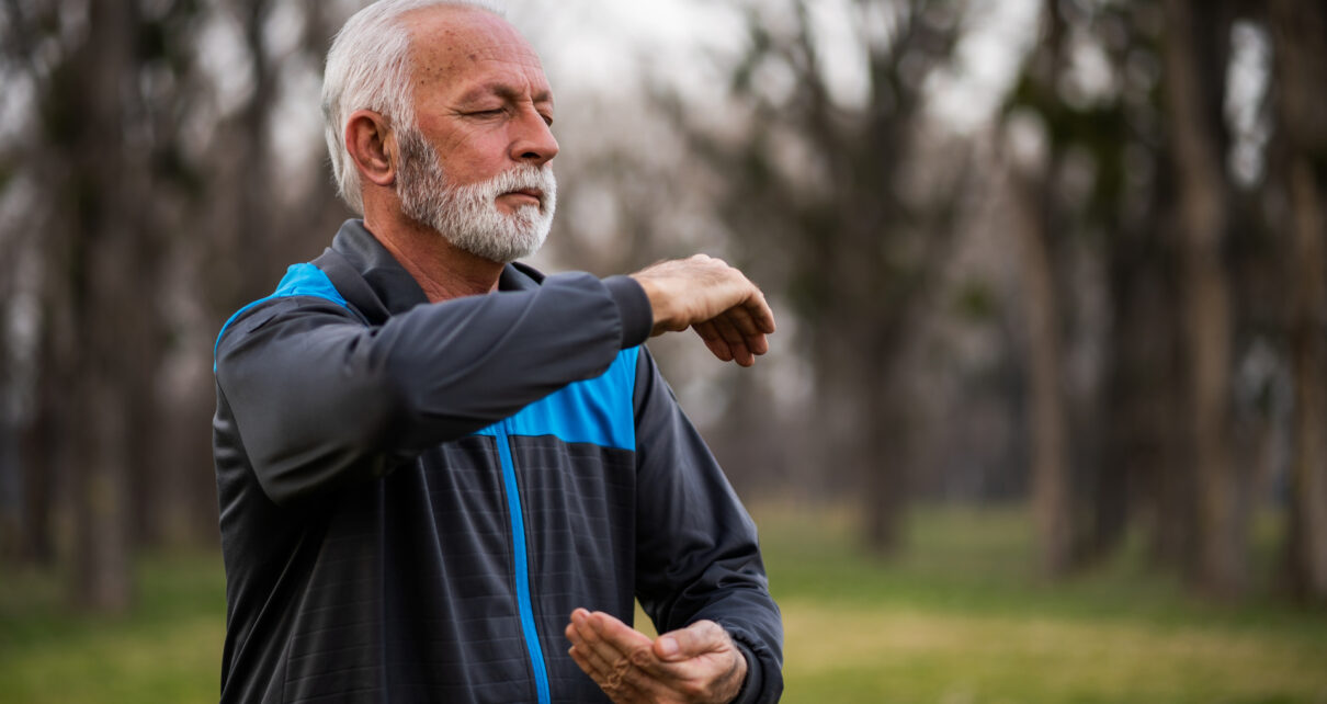 Na obrazku widać starszego mężczyznę ćwiczącego w parku na trawie. Pan wykonywany ćwiczenia skupiające się na wzmocnieniu mięśni pleców i brzucha oraz poprawie elastyczności kręgosłupa. W tle widać zielone drzewa i kwiaty, co nadaje temu miejscu spokojnego i relaksującego charakteru. Ćwiczący senior w parku to dobry przykład, jak ludzie starsi mogą dbać o swoje zdrowie i aktywność fizyczną, korzystając z otaczającej ich przyrody. Obrazek może stanowić inspirację dla osób starszych, które chcą zacząć ćwiczyć i dbać o swoje zdrowie na świeżym powietrzu w pięknych sceneriach.