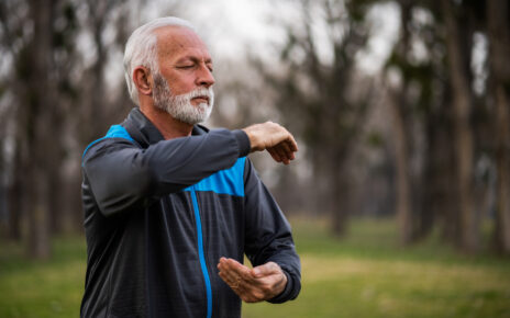Na obrazku widać starszego mężczyznę ćwiczącego w parku na trawie. Pan wykonywany ćwiczenia skupiające się na wzmocnieniu mięśni pleców i brzucha oraz poprawie elastyczności kręgosłupa. W tle widać zielone drzewa i kwiaty, co nadaje temu miejscu spokojnego i relaksującego charakteru. Ćwiczący senior w parku to dobry przykład, jak ludzie starsi mogą dbać o swoje zdrowie i aktywność fizyczną, korzystając z otaczającej ich przyrody. Obrazek może stanowić inspirację dla osób starszych, które chcą zacząć ćwiczyć i dbać o swoje zdrowie na świeżym powietrzu w pięknych sceneriach.