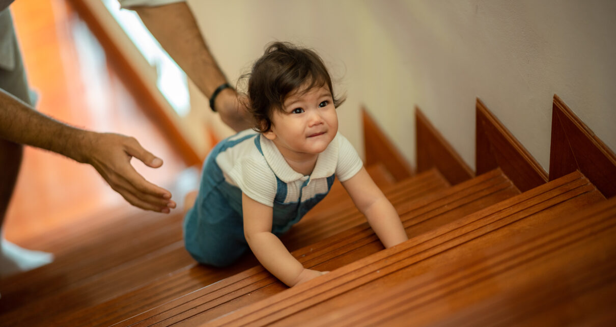 Na tym obrazku widoczne jest roczne dziecko, które pełne entuzjazmu wspina się po schodach. Z determinacją i umiejętnościami motorycznymi dziecko pokonuje kolejne stopnie, rozwijając swoją niezależność i zdolności fizyczne. Ta scena ilustruje ważny etap rozwoju dziecka oraz zdolność do samodzielnego poruszania się w przestrzeni