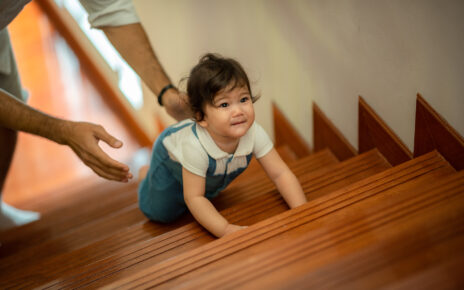 Na tym obrazku widoczne jest roczne dziecko, które pełne entuzjazmu wspina się po schodach. Z determinacją i umiejętnościami motorycznymi dziecko pokonuje kolejne stopnie, rozwijając swoją niezależność i zdolności fizyczne. Ta scena ilustruje ważny etap rozwoju dziecka oraz zdolność do samodzielnego poruszania się w przestrzeni
