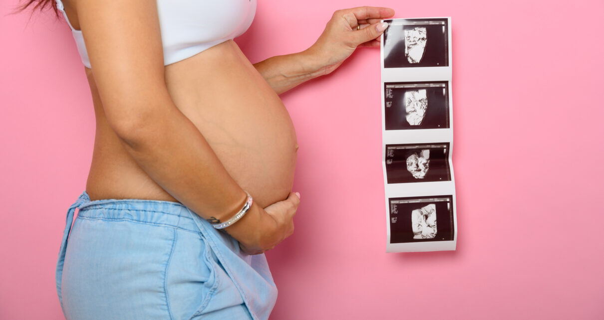 Na tym wzruszającym obrazku widzimy kobietę w ciąży, która trzyma przed sobą zdjęcia ultrasonograficzne swojego nienarodzonego dziecka. Jej spojrzenie jest pełne emocji i miłości, gdyż obrazki ukazują pierwsze wizualne połączenie z maleńkim życiem rozwijającym się w jej łonie. To piękna pamiątka i wyjątkowy sposób na zbliżenie się do swojego dziecka jeszcze przed jego narodzinami